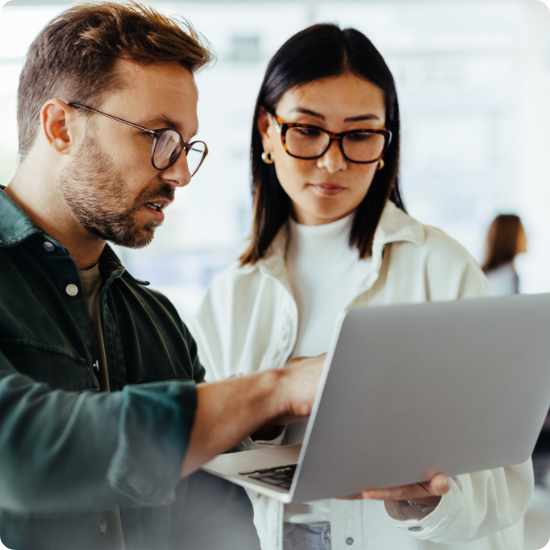 Two colleagues, a man and a woman, collaborate closely on a laptop, their focused expressions and shared gaze suggesting a serious and productive work environment.