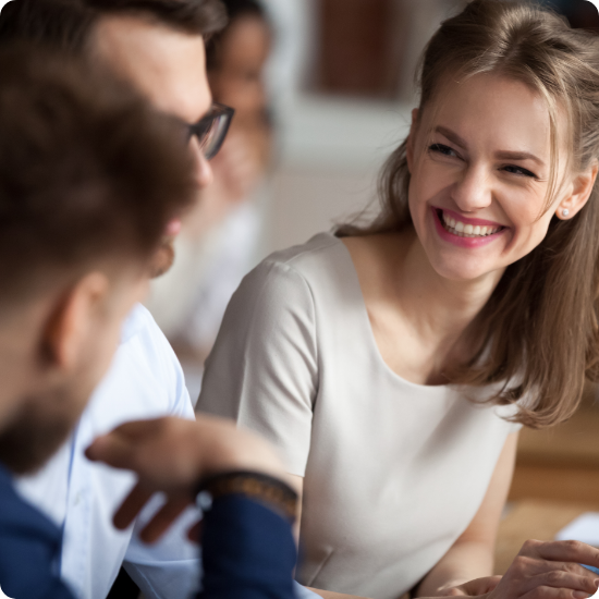 A woman smiles while seated at a table with two men, creating a warm and friendly atmosphere.