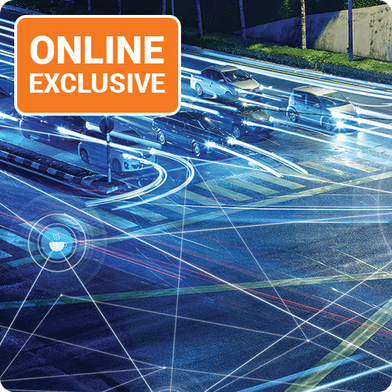 A street scene featuring several cars parked and driving along the road under a clear blue sky.