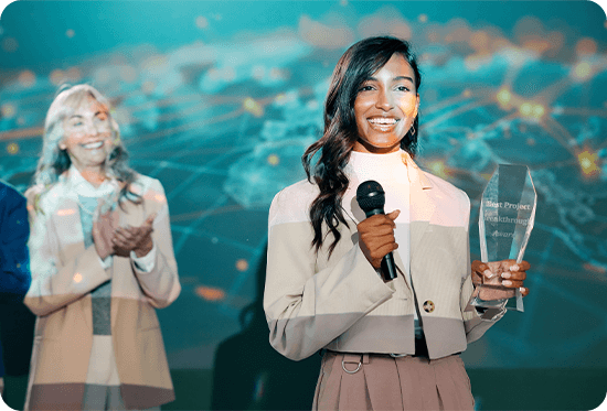 A young woman joyfully accepts an award onstage, while a woman in the background applauds, creating a celebratory and positive atmosphere.