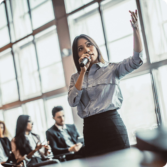 A woman with a microphone speaking to guests in an office